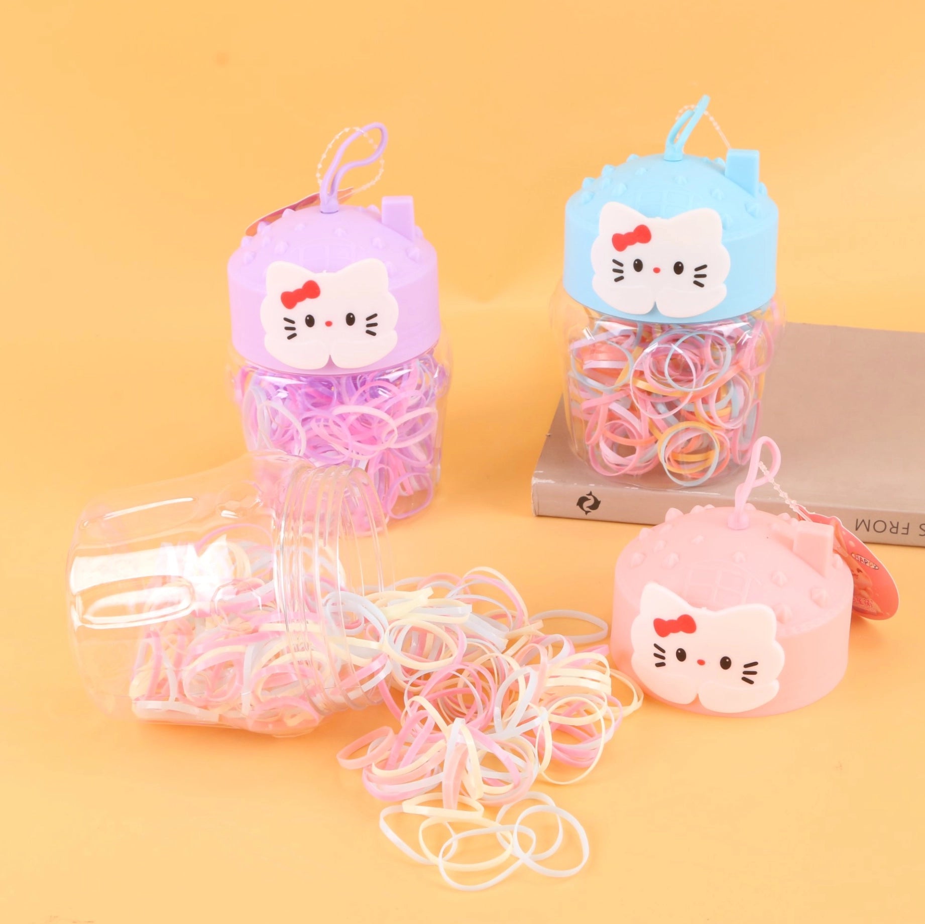 fondo tomate con  Ligas de colores desechables para cabello en frasco decorativo con tapa en forma de gato. Caja de 24, ideal para tiendas y mayoristas.