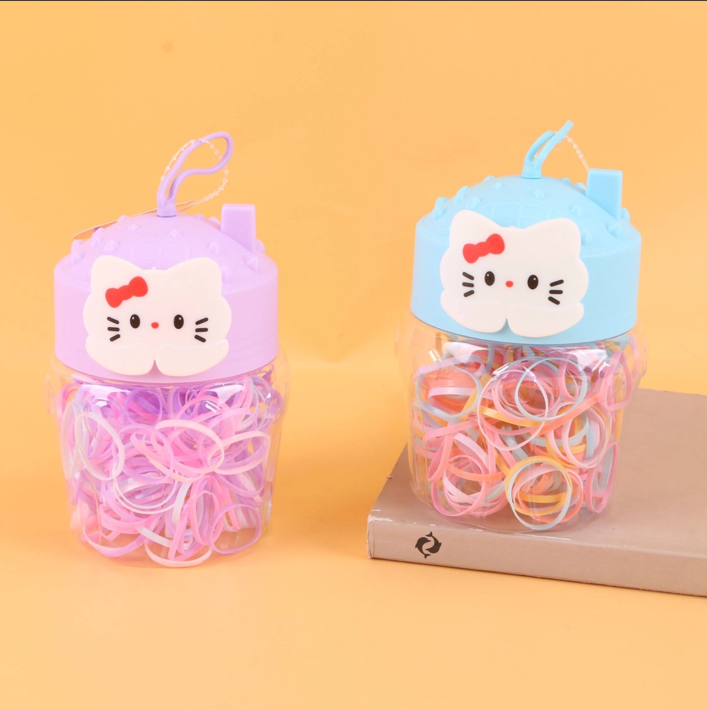 fondo tomate con  Ligas de colores desechables para cabello en frasco decorativo con tapa en forma de gato. Caja de 24, ideal para tiendas y mayoristas.